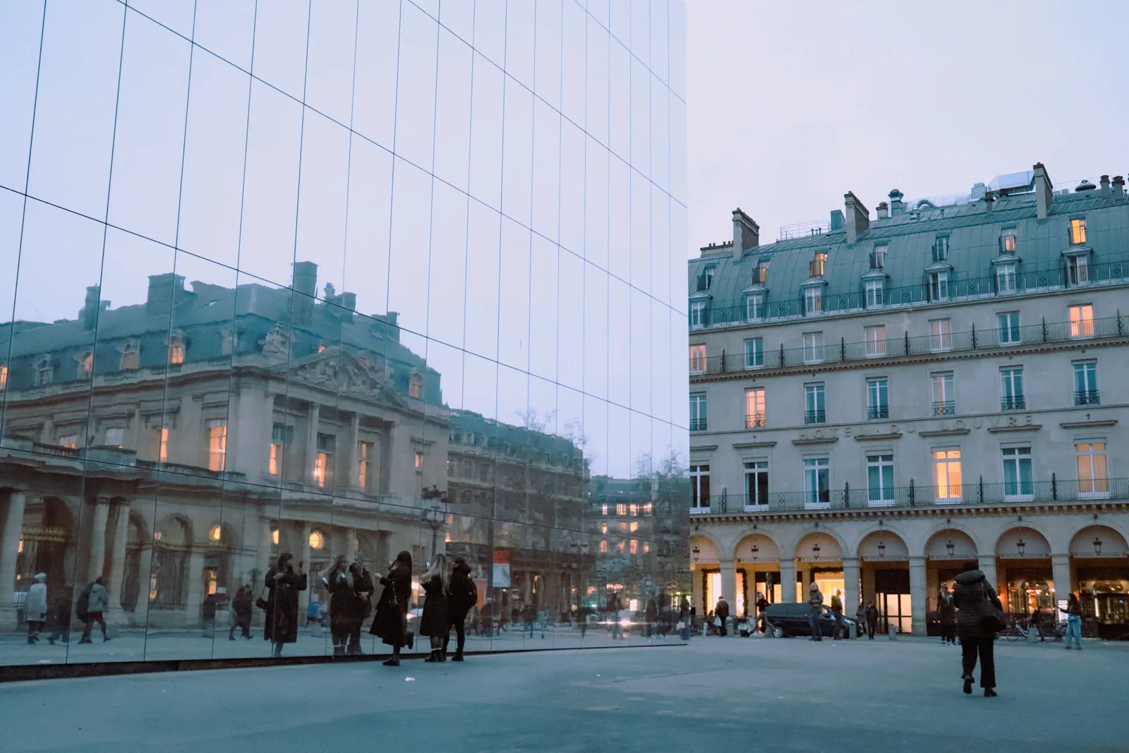 Un immeuble haussmannien illuminé et son reflet dans un mur de miroirs, près du Palais-Royal, à la tombée du jour